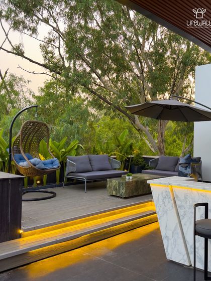 This lounge area is designed for ultimate comfort, with deep-seated sofas, a hanging wicker swing chair, and a backdrop of lush greenery, making it feel like a resort escape.