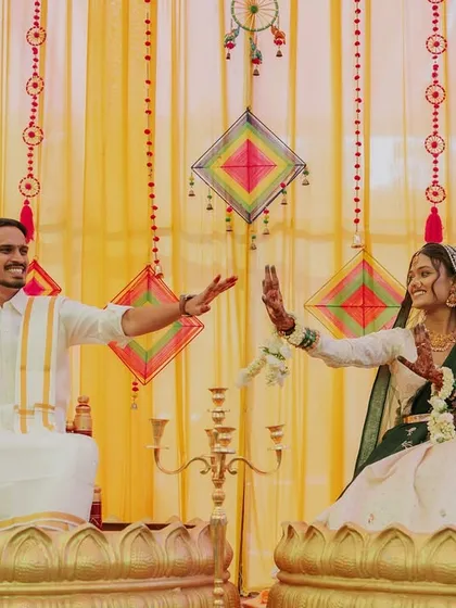 The happy couple strikes a pose during their Haldi ceremony, seated in decorative pots against a colorful backdrop.