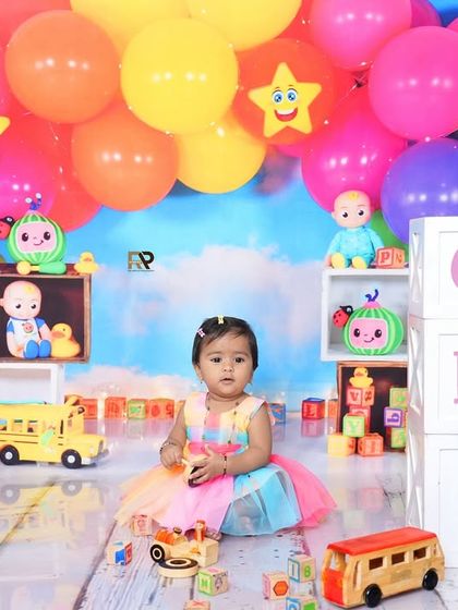 A full view of the Cocomelon setup, with a baby girl sitting happily among the toys and balloons. The "ONE" blocks are perfect for a first birthday celebration.
