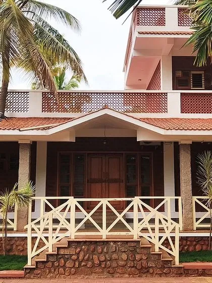 A close-up of the farmhouse facade, highlighting the texture of the laterite blocks and the simple, elegant design of the wooden railings.