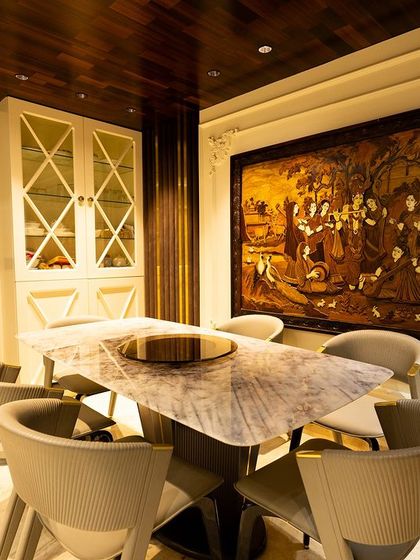 A dining area that blends modern comfort with traditional art. The sleek chairs and marble table are juxtaposed with a large, intricate wood-carved artwork, creating a unique focal point.
