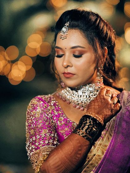 My dear client Spoorthi looks like a doll in this classic South Indian bridal look. Her rich purple and gold Kanchipuram saree is paired with a pink blouse featuring delicate hand embroidery, perfect for her wedding ceremony.