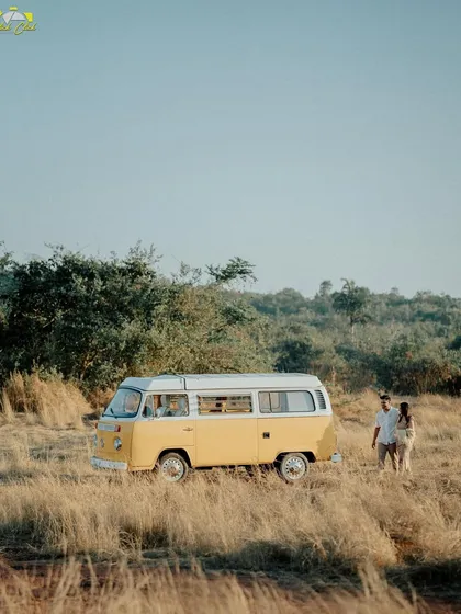 A wide shot showing the couple and their vintage van in a vast, rustic field in Goa, creating a sense of adventure and freedom.