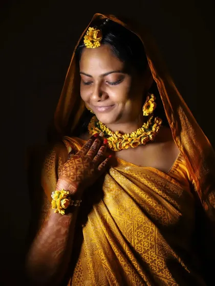 Another beautiful low-light portrait of the bride at her Haldi. The soft lighting highlights her gentle smile and the traditional floral jewelry, capturing a moment of quiet happiness.