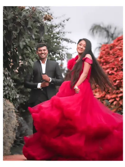 A candid, joyful moment captured in a beautiful garden setting. The bride's flowing red dress adds a vibrant splash of colour, and her natural smile is the focus of this pre-wedding portrait.