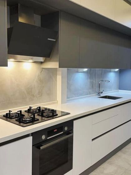 A close-up of the cooking area, featuring a four-burner hob and a built-in oven below. The minimalist chimney hood fits perfectly within the sleek grey upper cabinets.