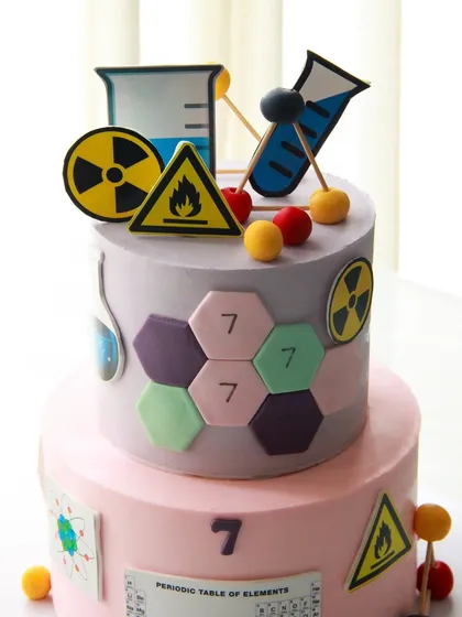 A fun, two-tiered science-themed cake for a 7th birthday, decorated with beakers, warning signs, and the periodic table.