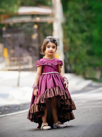 A full-length portrait of a little girl in a stunning purple gown, posing on the street for her third birthday photoshoot.