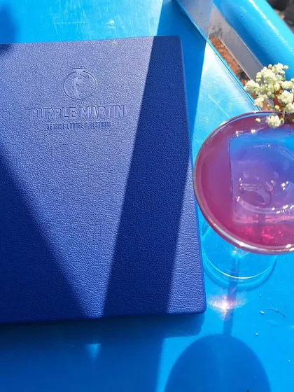 A signature cocktail from Purple Martini, served against the backdrop of the blue sea.