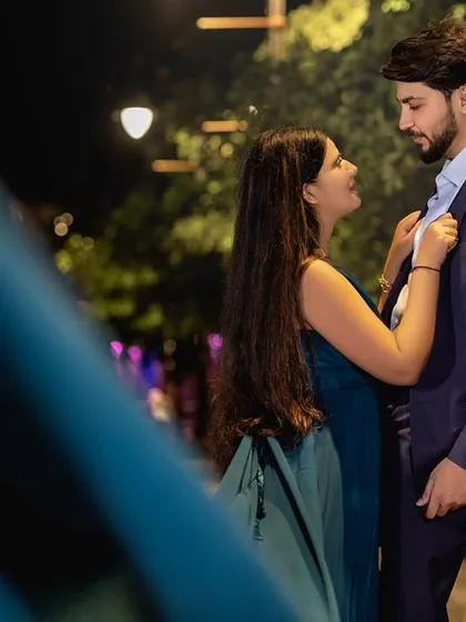 A playful, intimate moment by a lamppost. The composition uses the foreground to create a sense of peeking into a private, romantic conversation between the couple.
