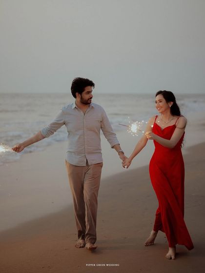 Holding hands and walking along the shore with sparklers, this image captures the playful and romantic energy of a pre-wedding beach shoot.