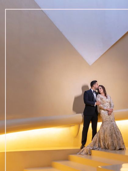 A modern, architectural portrait of the couple. John's gentle kiss on Jahanvi's forehead against the clean lines and warm light of the venue creates a sophisticated and romantic image.