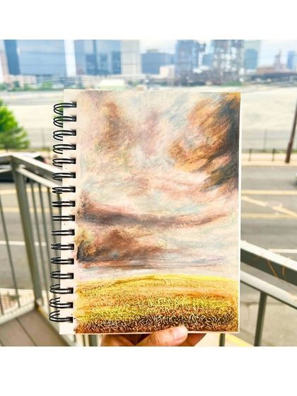 A landscape sketch in a spiral-bound notebook, created with oil pastels against a city backdrop. We teach you how to find inspiration anywhere.