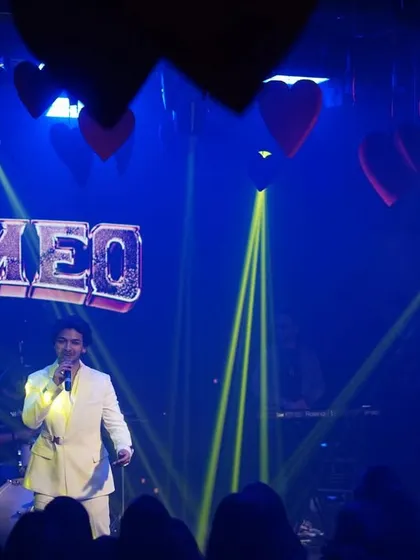 A concert stage setup for a sangeet night, featuring a custom "Rromeo" marquee sign, professional spotlights, and hanging heart props to match the romantic theme.
