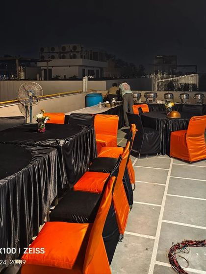 The seating arrangement for a terrace Diwali party, with round tables and chairs covered in black and orange fabric.