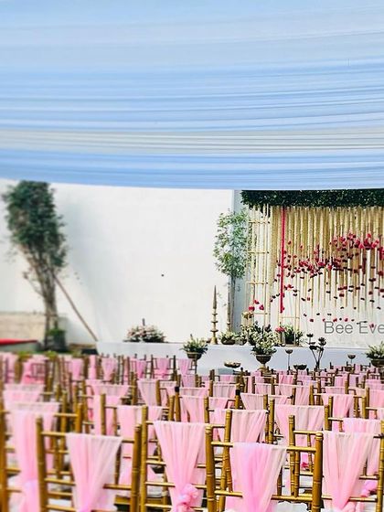 A beautiful outdoor wedding setup with pink-draped chairs leading to an elegant floral stage. The open-air setting and the soft color palette create a romantic and dreamy atmosphere.