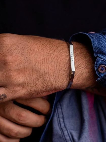 A man with hand tattoos wearing a black engraved cuff, paired with a denim shirt. The bracelet adds a sleek, modern edge to his rugged style.