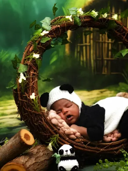 A full view of the sleeping panda newborn in the vine wreath, surrounded by a lush green forest backdrop.