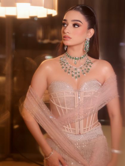 A profile shot that showcases the wet-look hairstyle and the beautiful layering of the emerald necklaces.