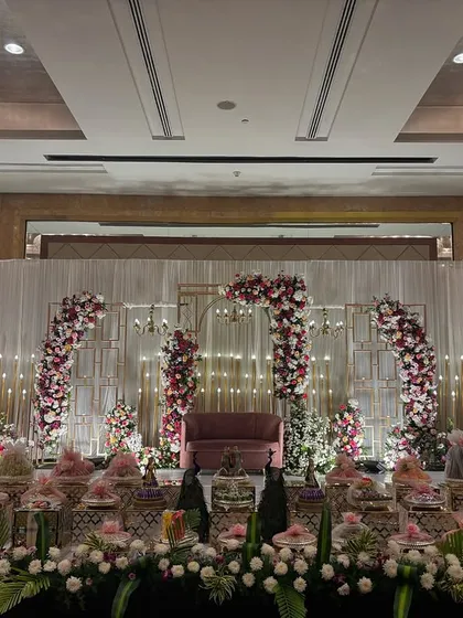 A contemporary stage with geometric gold arches adorned with red and pink flowers, set against a white curtain backdrop.