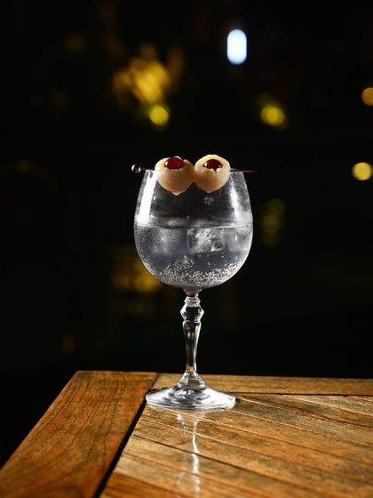 A celebratory cocktail for our second anniversary, garnished with lychees and set against the sparkling lights of the resort at night.