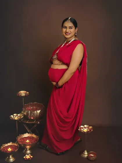 A beautiful standing portrait showcasing the full drape of the red saree, surrounded by festive diyas that add warmth and glow.