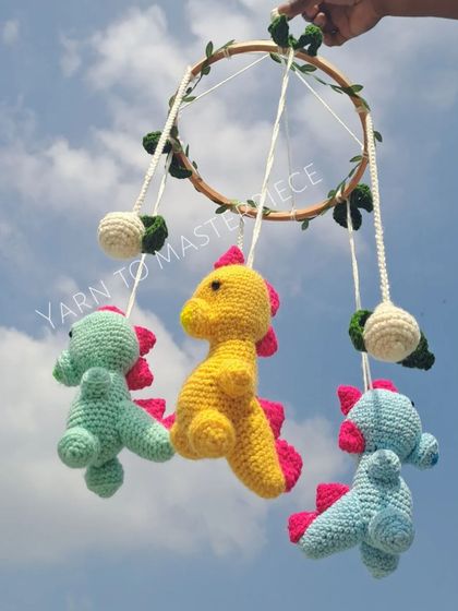 A playful dinosaur-themed cradle mobile. Three friendly dinosaurs in bright colors hang from a leafy hoop, ready to spark your baby's imagination.