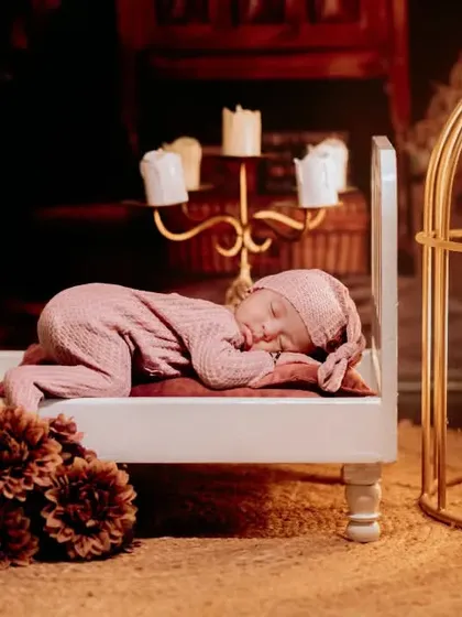 An artistic newborn portrait with the baby sleeping on a miniature bed, set against a warm, candlelit backdrop for a dreamy effect.