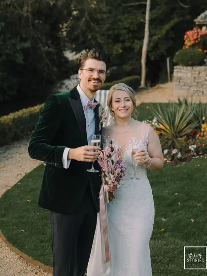 A happy portrait of the couple, holding champagne glasses and smiling at the camera during their UK countryside wedding.