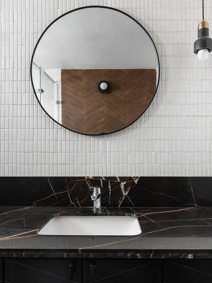A modern bathroom design featuring a sleek black marble countertop with dramatic gold veining. We paired it with a simple round mirror and minimalist white tiles for a look that is clean and sophisticated.
