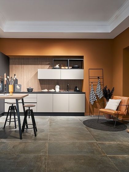 An earthy terracotta wall color provides a warm and inviting backdrop for this kitchen, which combines dark grey and light beige cabinets for a layered, modern look.