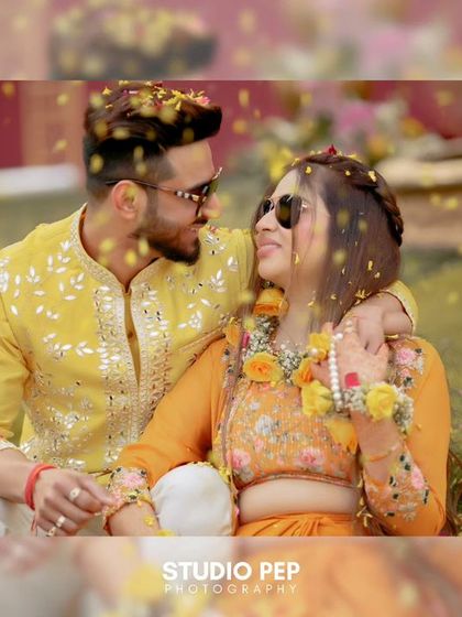 A romantic shot of the couple amidst a shower of flower petals, their sunglasses adding a cool, modern twist to the traditional Haldi look.