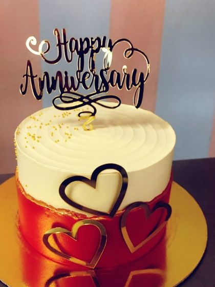 A slightly different angle of the red and white anniversary cake, showing the swirled frosting on top and the placement of the golden "Happy Anniversary" topper.
