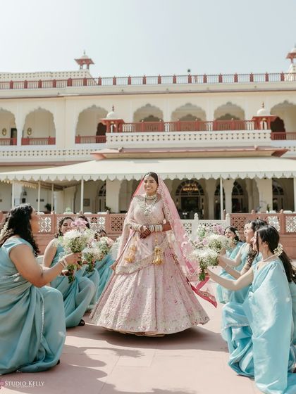 The bride makes her grand entrance, flanked by her bridesmaids in matching blue sarees, creating a beautiful and coordinated bridal procession.