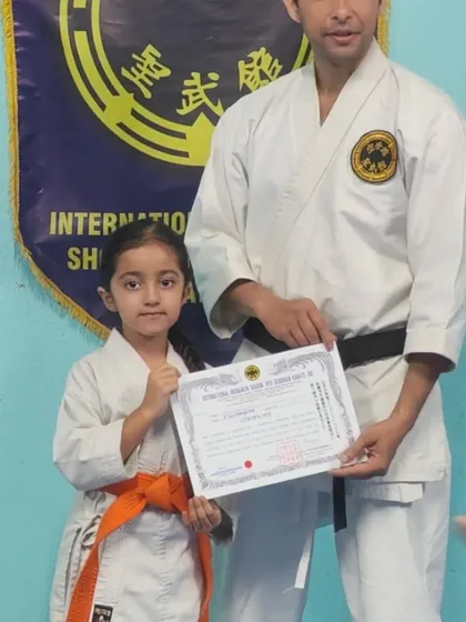 A young girl proudly holds her 7th Kyu (orange belt) certificate. Her focus and fist show the spirit of a true karateka.