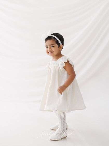 A classic portrait of the birthday girl. The simple white dress and background create a timeless look, while her happy expression captures the spirit of her second birthday.