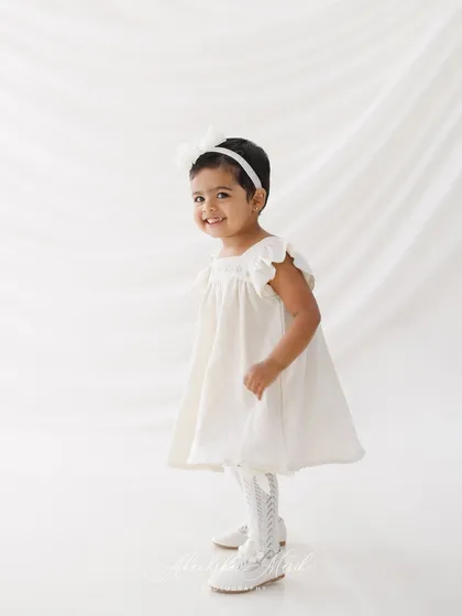 A classic portrait of the birthday girl. The simple white dress and background create a timeless look, while her happy expression captures the spirit of her second birthday.