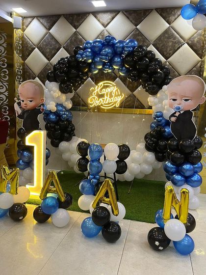 This is a duplicate of ID 30, 95, 208, 220, 248. A classic Boss Baby theme for a first birthday. This setup includes a balloon arch in blue, black, and white, character cutouts, a 'Happy Birthday' neon sign, and a light-up number '1'.