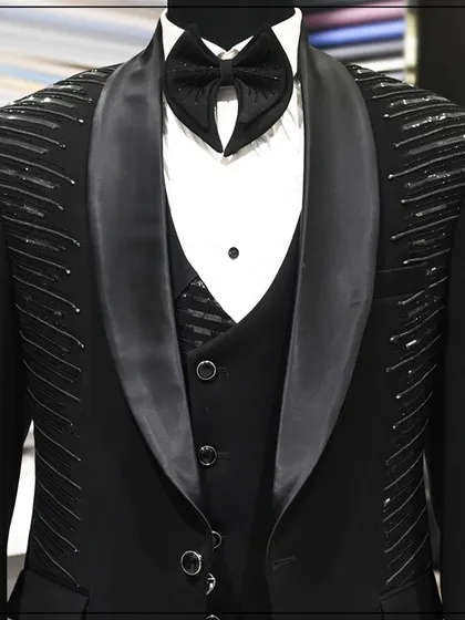 A full look at a black three-piece tuxedo with linear silver embroidery on the shoulders and lapels. The design is modern and architectural, perfect for a fashion-forward client.