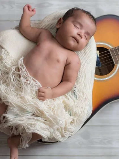 We create timeless and creative portraits that tell your family's story. Here, a newborn sleeps peacefully, nestled safely against a family guitar, turning a personal item into a beautiful part of their first photoshoot. This is a perfect example of our personalized studio sessions in Gurugram.