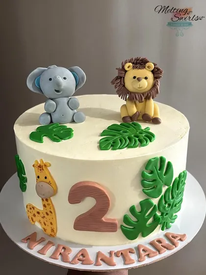 A simple and cute jungle-themed cake perfect for a second birthday. This design features adorable, handmade fondant animals like an elephant, lion, and giraffe on a clean, white whipped cream base.