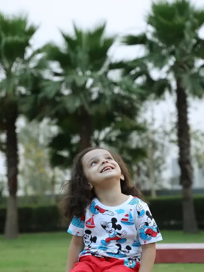 A beautiful portrait of a child looking up with a happy expression. The natural light and green background of the park create a perfect setting for kids' photography.
