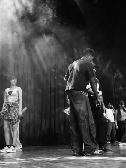 A dramatic black and white shot from behind the scenes, with stage lights creating a powerful silhouette. This captures the focus before the show.