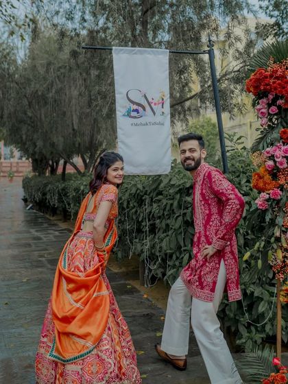 A fun moment with the couple posing next to their custom wedding signage and a vibrant floral arch.