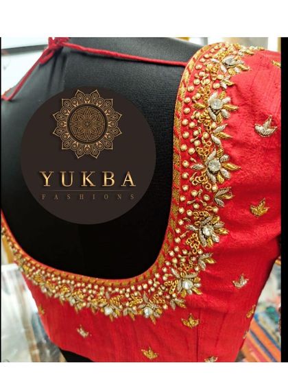 A classic red bridal blouse with a deep U-neck. The neckline is heavily embellished with gold zardosi and white beadwork in a floral pattern.