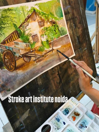 The artist's hand and palette are in focus here, showing the mixing of colors before they are applied to the rustic landscape painting.