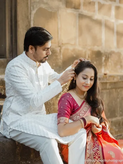 A tender and romantic moment. The groom gently places a flower in the bride's hair as they sit on ancient stone steps, creating a scene that is both sweet and timeless.