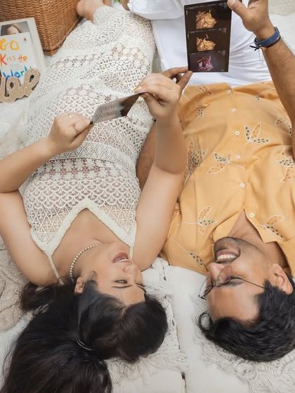 A fun and creative aerial shot of a couple at their picnic. They lie on their backs, holding up their sonogram picture to the camera, sharing their excitement.