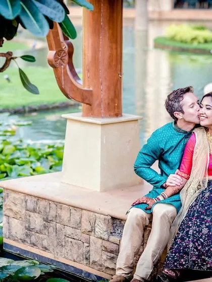A fun, behind-the-scenes style shot showing the reality of a photoshoot. While the couple shares a sweet kiss, family members can be seen in the background, adding a touch of humor and reality.