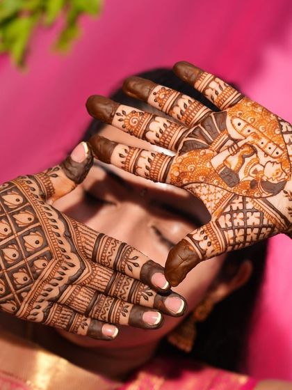 A creative shot of a bride making a heart shape with her hands, with the focus on the intricate details of the henna.